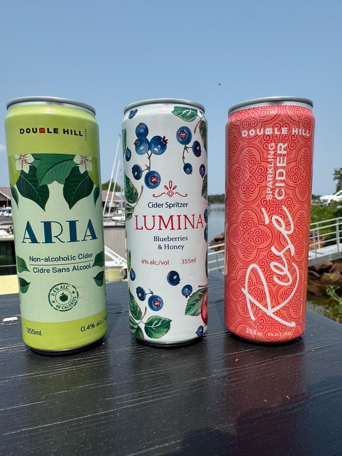 Double Hill Cidery cans — Aria, Lumina, and Rosé — on a sunny dock