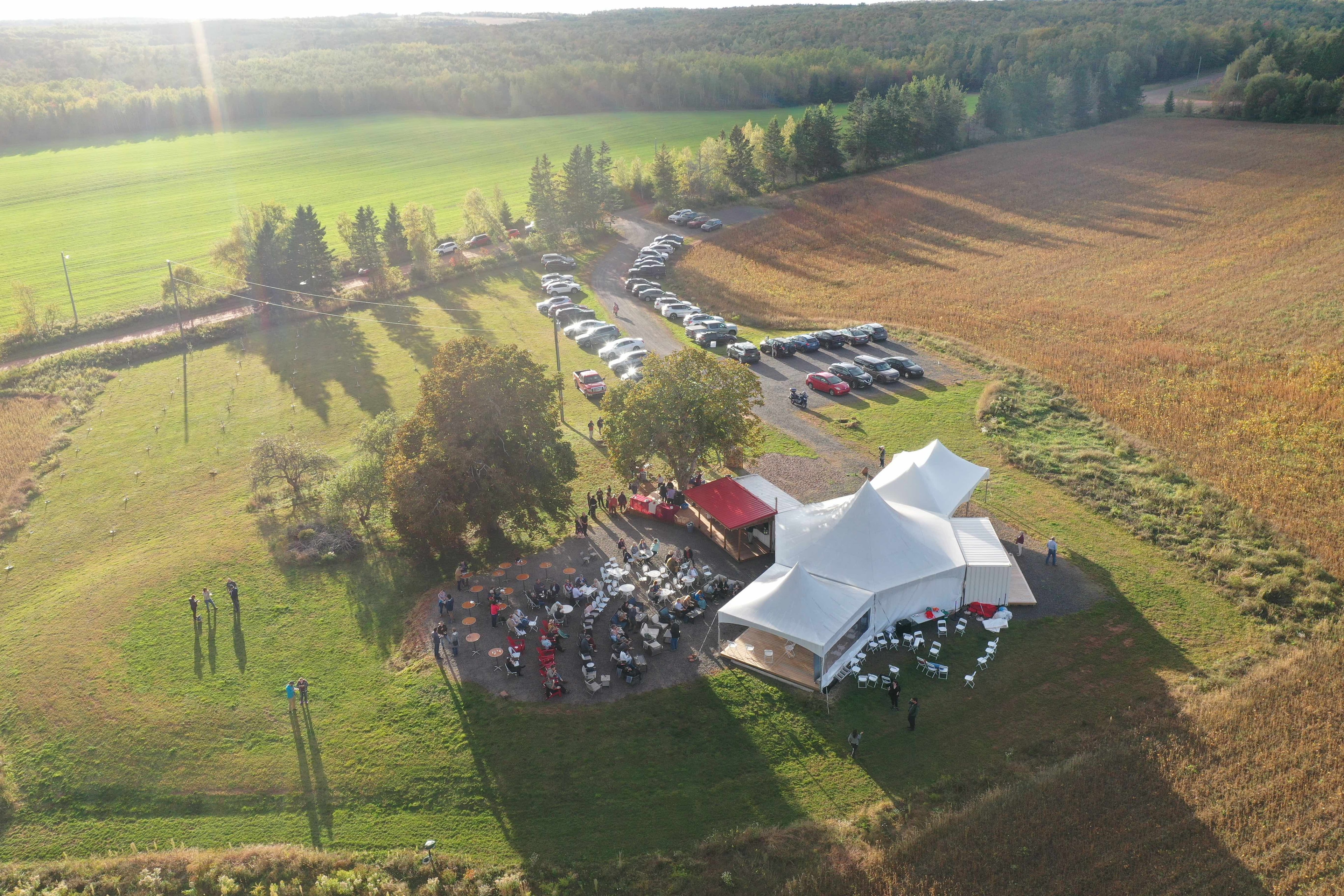 Guests dining at a long outdoor table at golden hour overlooking the PEI landscape